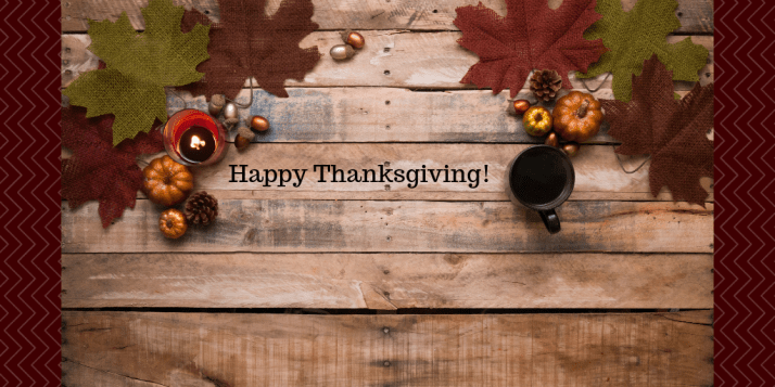 Wooden table with fall leaves, candle, mug sitting on it and the words Happy Thanksgiving written on it